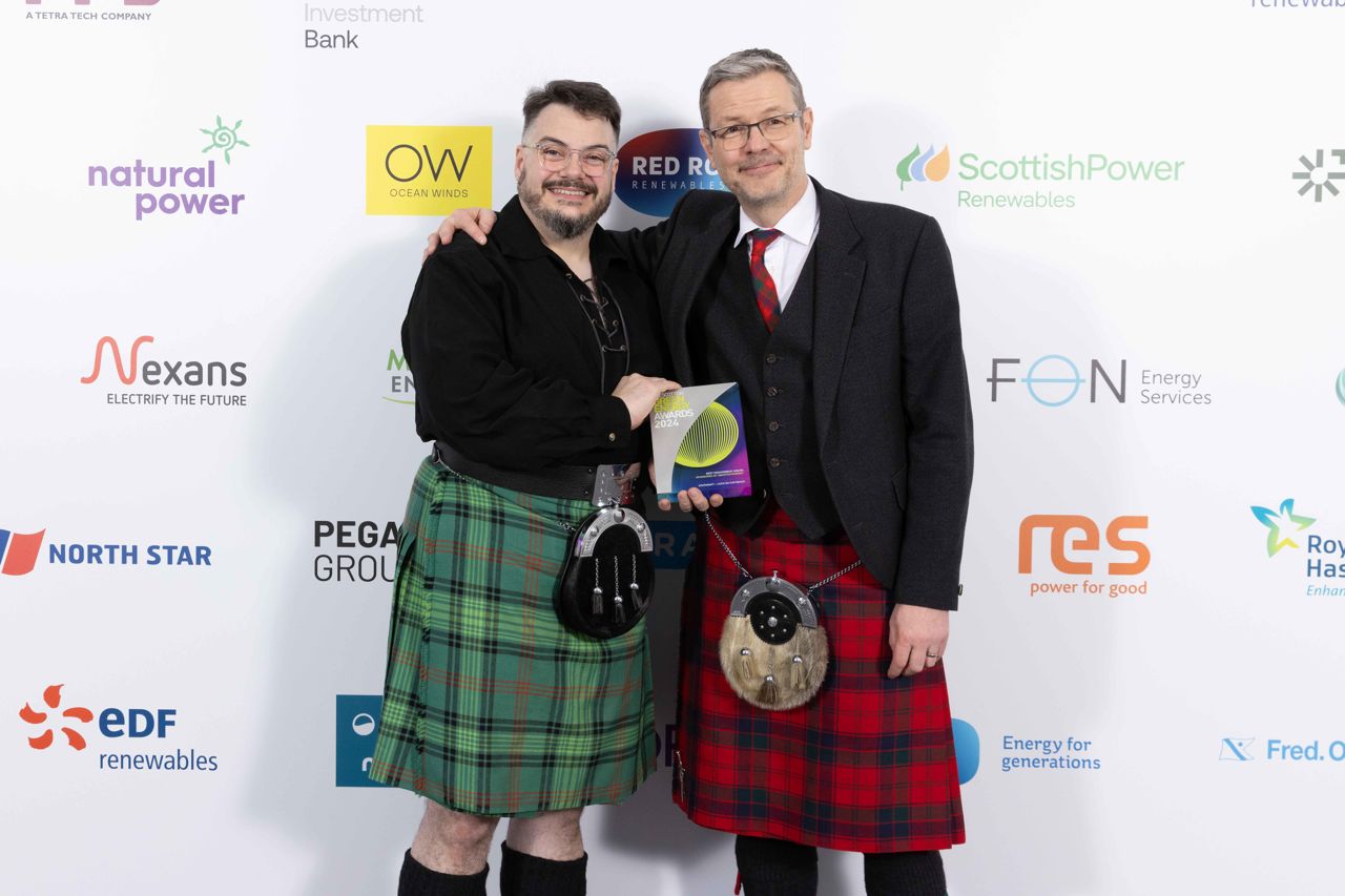 Two men stand together holding a trophy award